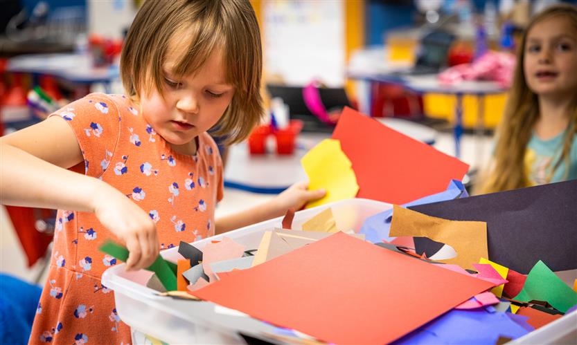 A girl wearing a pink shirt picks out construction paper from a pile of scraps